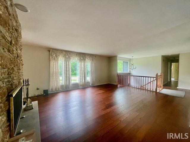 unfurnished living room featuring wood finished floors, a fireplace, a chandelier, and baseboards