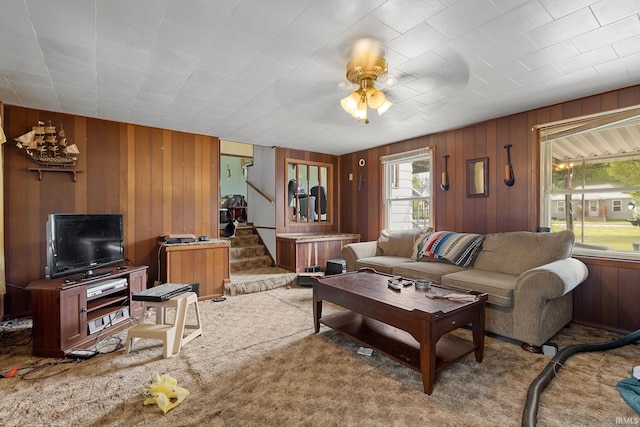 carpeted living room with wood walls, stairs, and ceiling fan