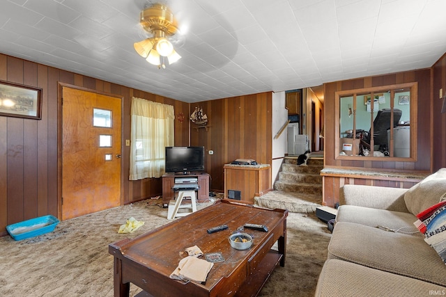 living area featuring carpet flooring, wooden walls, ceiling fan, and stairway