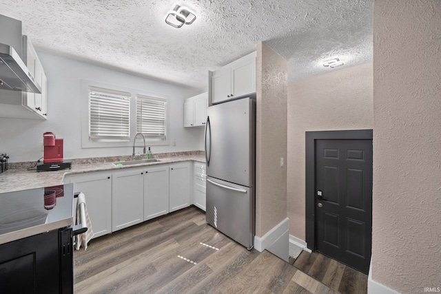 kitchen with freestanding refrigerator, a sink, dark wood-style flooring, wall chimney range hood, and light countertops