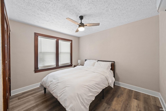 bedroom with a textured ceiling, baseboards, a wall unit AC, wood finished floors, and ceiling fan