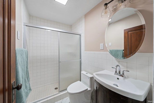 full bathroom featuring a stall shower, toilet, tile walls, wainscoting, and vanity