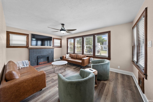 living area with a ceiling fan, a textured ceiling, a brick fireplace, wood finished floors, and plenty of natural light