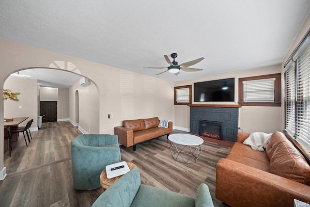 living room with arched walkways, a glass covered fireplace, a ceiling fan, and wood finished floors