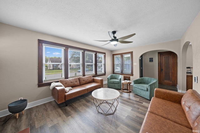living room with arched walkways, ceiling fan, wood finished floors, baseboards, and a textured ceiling