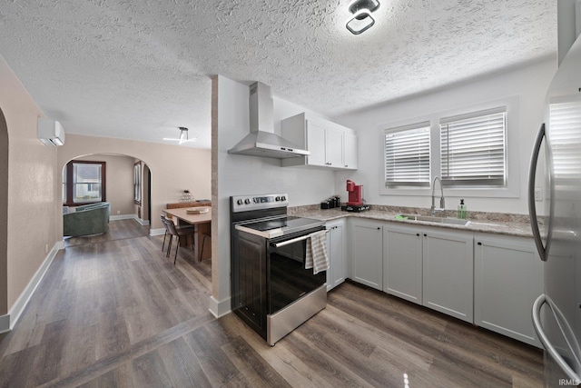 kitchen featuring stainless steel appliances, wall chimney range hood, a sink, arched walkways, and a textured ceiling