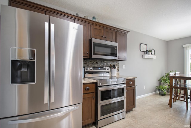 kitchen featuring stainless steel appliances, tasteful backsplash, baseboards, dark brown cabinets, and light stone counters