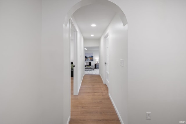 hall featuring light wood-style floors, arched walkways, recessed lighting, and baseboards