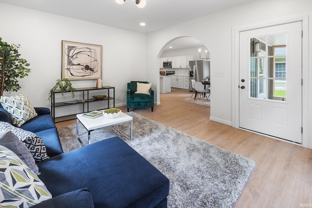 living area featuring arched walkways, light wood-type flooring, recessed lighting, and baseboards
