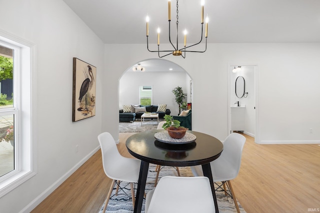 dining room with arched walkways, light wood-style floors, baseboards, and a chandelier