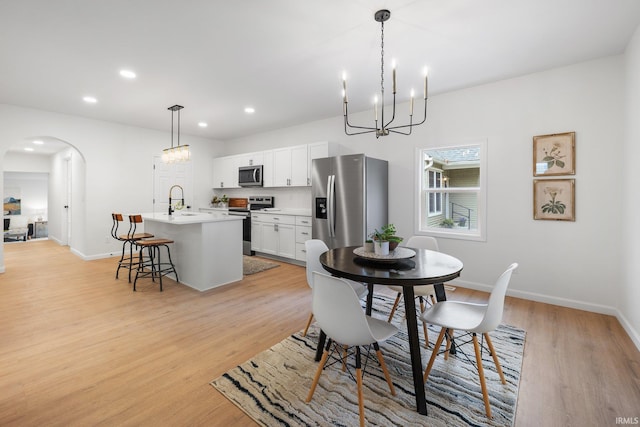 dining space with a chandelier, arched walkways, baseboards, light wood-style floors, and recessed lighting