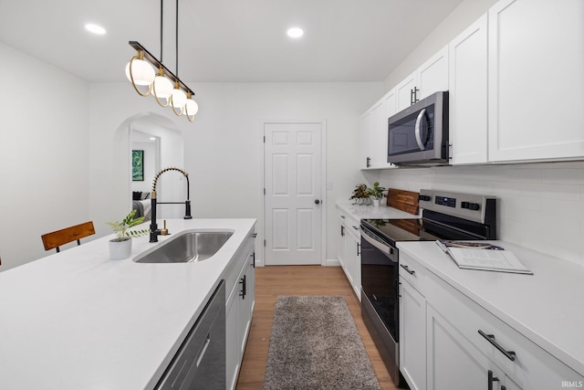 kitchen with appliances with stainless steel finishes, a sink, wood finished floors, light countertops, and recessed lighting