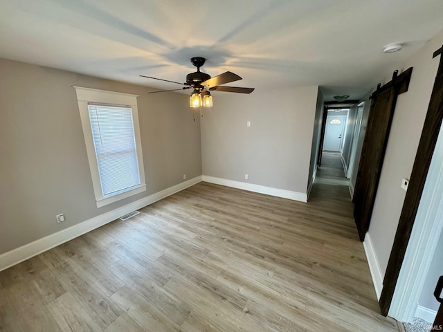 unfurnished bedroom with a barn door, baseboards, light wood-style floors, and a ceiling fan