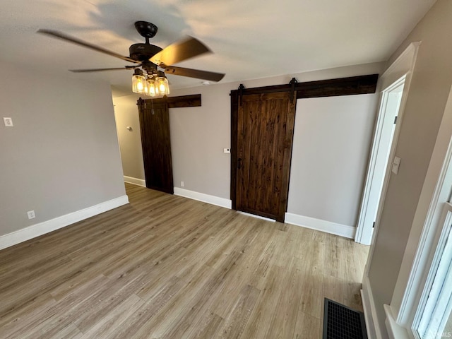 unfurnished bedroom featuring a barn door, light wood finished floors, baseboards, and ceiling fan
