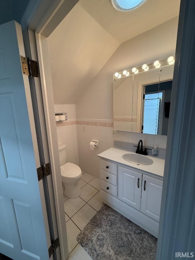 bathroom featuring lofted ceiling, tile walls, toilet, vanity, and tile patterned floors