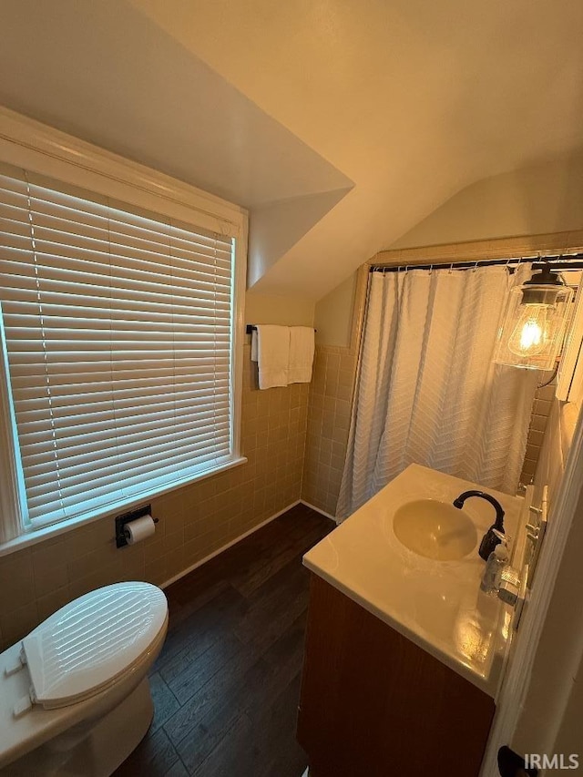 bathroom featuring tile walls, wood finished floors, vanity, toilet, and lofted ceiling
