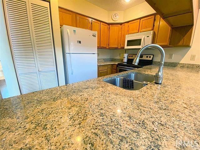 4068 E Eagle Bay Dr Unit 46, Bloomington, IN 47401 - kitchen featuring white appliances, brown cabinets, light stone counters, a sink, and a peninsula