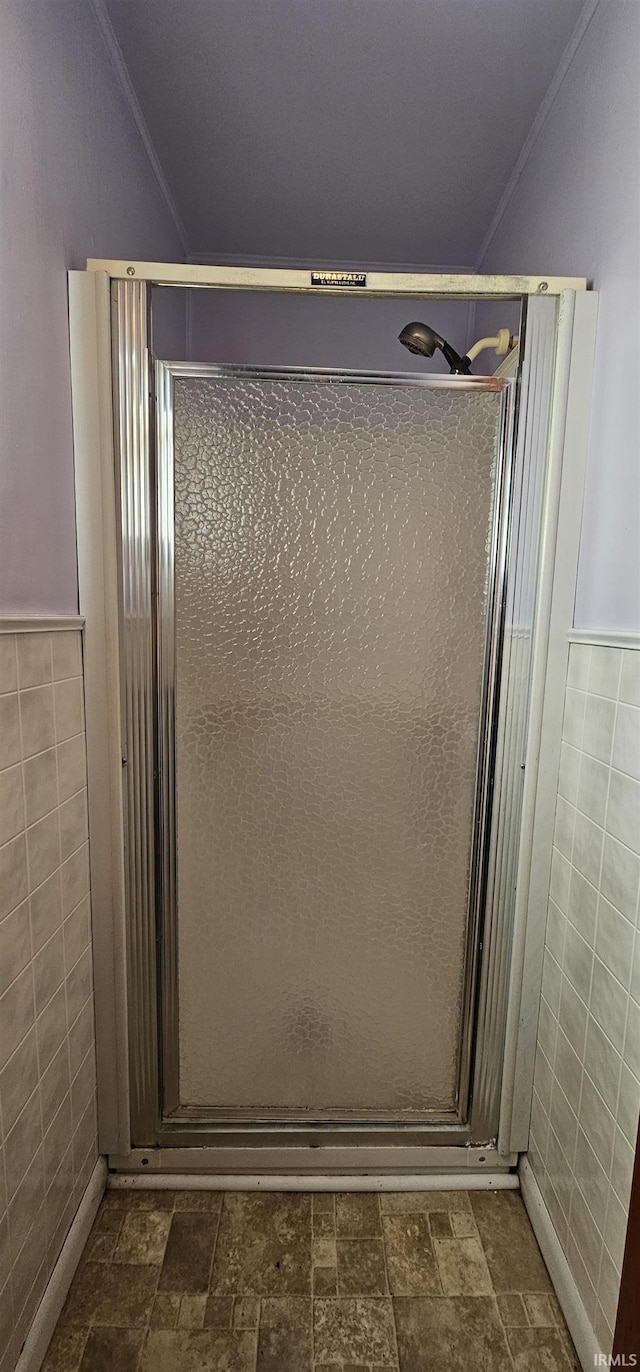 full bathroom featuring tile walls, a shower stall, a wainscoted wall, and stone finish floors
