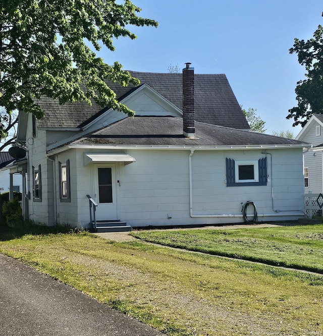 view of side of property featuring entry steps, a yard, a chimney, and roof with shingles