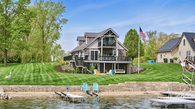 rear view of property featuring stairway, a balcony, stone siding, a lawn, and a deck with water view