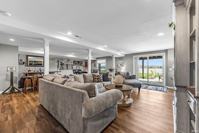 living room featuring bar area, ornate columns, recessed lighting, a textured ceiling, and dark wood-style floors