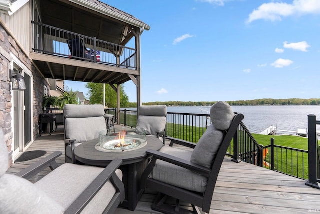 deck with an outdoor fire pit, a water view, and a lawn