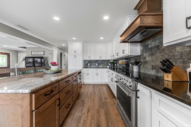 kitchen with custom range hood, dark stone countertops, white cabinetry, light wood-type flooring, and recessed lighting