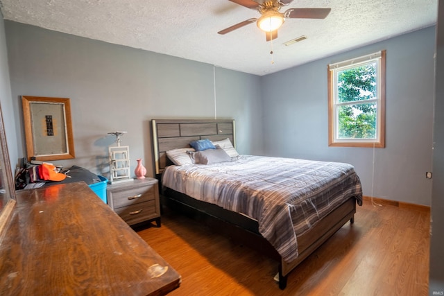 bedroom with light wood-type flooring, a textured ceiling, a ceiling fan, and baseboards