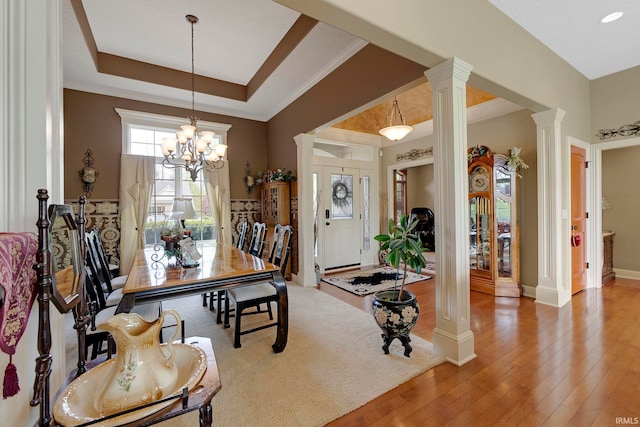 dining room featuring ornate columns, hardwood / wood-style flooring, a chandelier, baseboards, and ornamental molding