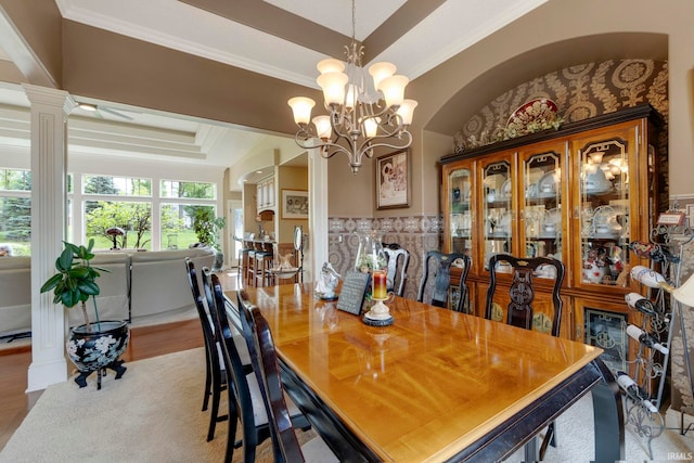 dining area with decorative columns, a raised ceiling, ornamental molding, and a chandelier