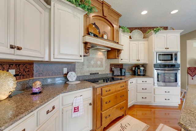 kitchen featuring stainless steel appliances, light wood-style floors, decorative backsplash, light stone countertops, and a textured ceiling
