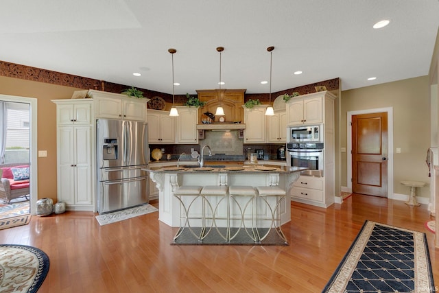 kitchen featuring appliances with stainless steel finishes, tasteful backsplash, light wood finished floors, a kitchen breakfast bar, and baseboards