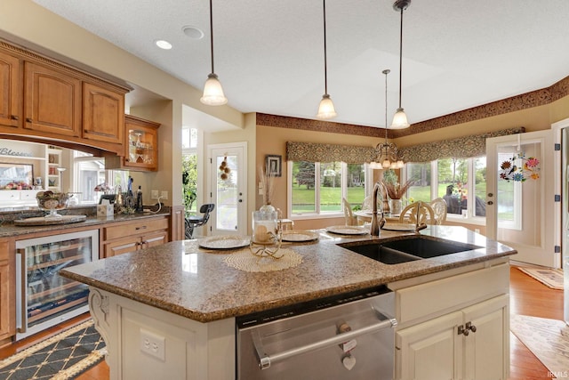 kitchen with stainless steel dishwasher, beverage cooler, a sink, an island with sink, and light stone countertops