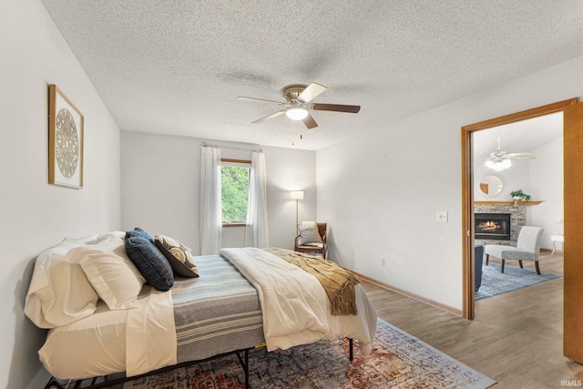 6114 Picacho Dr, Fort Wayne, IN 46825 - bedroom with wood finished floors, a warm lit fireplace, a textured ceiling, and a ceiling fan