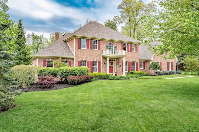 10528 Indian Ridge Dr, Fort Wayne, IN 46814 - colonial-style house with a chimney, brick siding, a front yard, a shingled roof, and a balcony