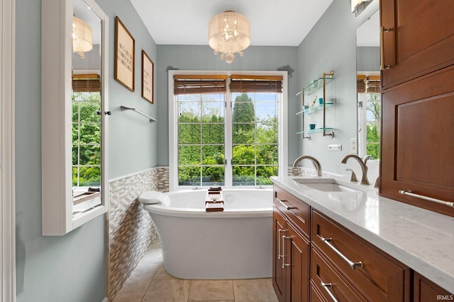 bathroom with plenty of natural light, tile patterned flooring, a soaking tub, vanity, and a wainscoted wall