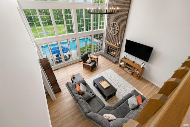 living area featuring a chandelier, a brick fireplace, wood finished floors, and a high ceiling