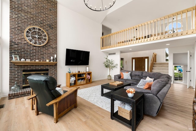 living room with a high ceiling, baseboards, wood finished floors, stairs, and a brick fireplace