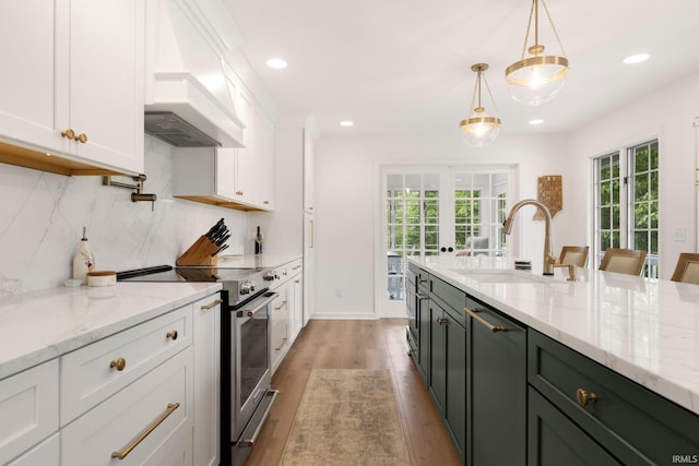 kitchen with stainless steel appliances, premium range hood, a sink, white cabinets, and plenty of natural light