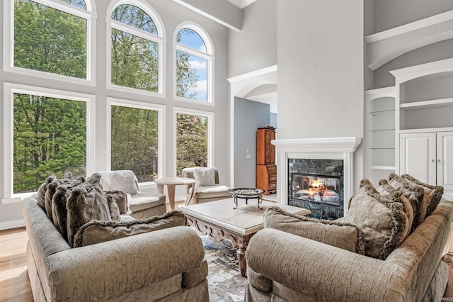 living room with a towering ceiling, a premium fireplace, arched walkways, wood finished floors, and built in features