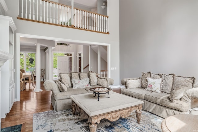 living area with decorative columns, a high ceiling, wood finished floors, and baseboards