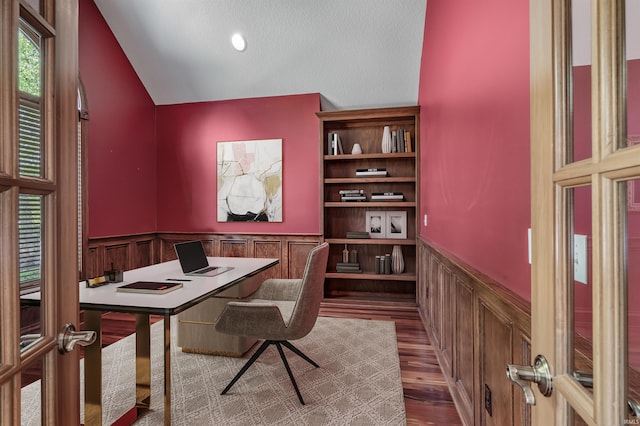 office area with wainscoting, vaulted ceiling, wood finished floors, and a decorative wall