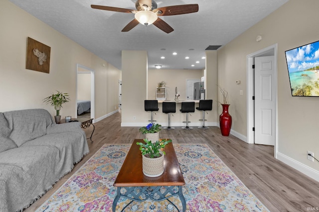 living area with a ceiling fan, light wood finished floors, baseboards, recessed lighting, and a textured ceiling