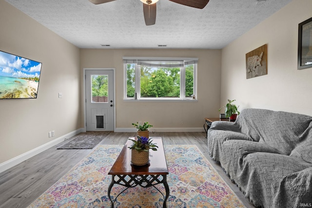 living room with a ceiling fan, wood finished floors, baseboards, and a textured ceiling