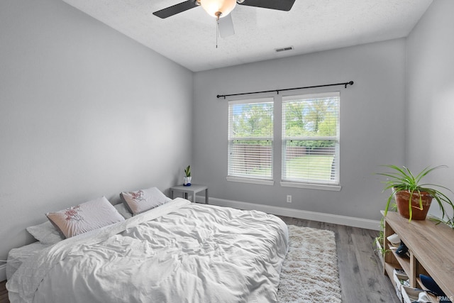 bedroom with a textured ceiling, wood finished floors, baseboards, and a ceiling fan