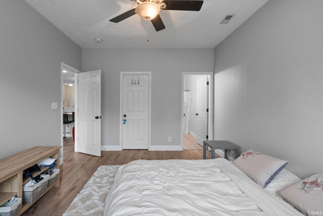 bedroom featuring wood finished floors, ceiling fan, baseboards, and ensuite bathroom
