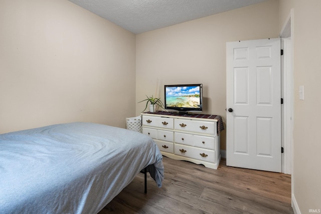 bedroom featuring wood finished floors, a textured ceiling, and baseboards