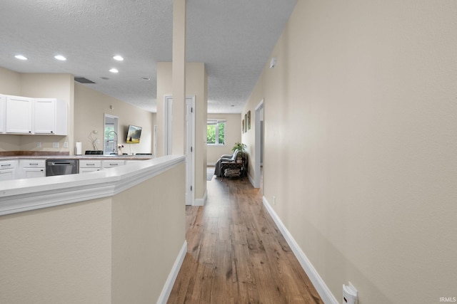 hall with a textured ceiling, light wood finished floors, baseboards, and recessed lighting