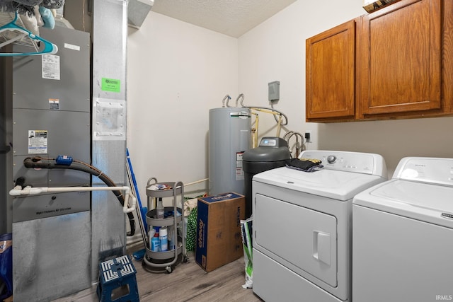 laundry room featuring cabinet space, washing machine and dryer, electric water heater, light wood-style flooring, and heating unit