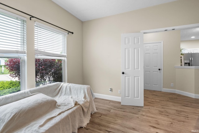 bedroom featuring stainless steel fridge with ice dispenser, light wood-style flooring, multiple windows, and baseboards
